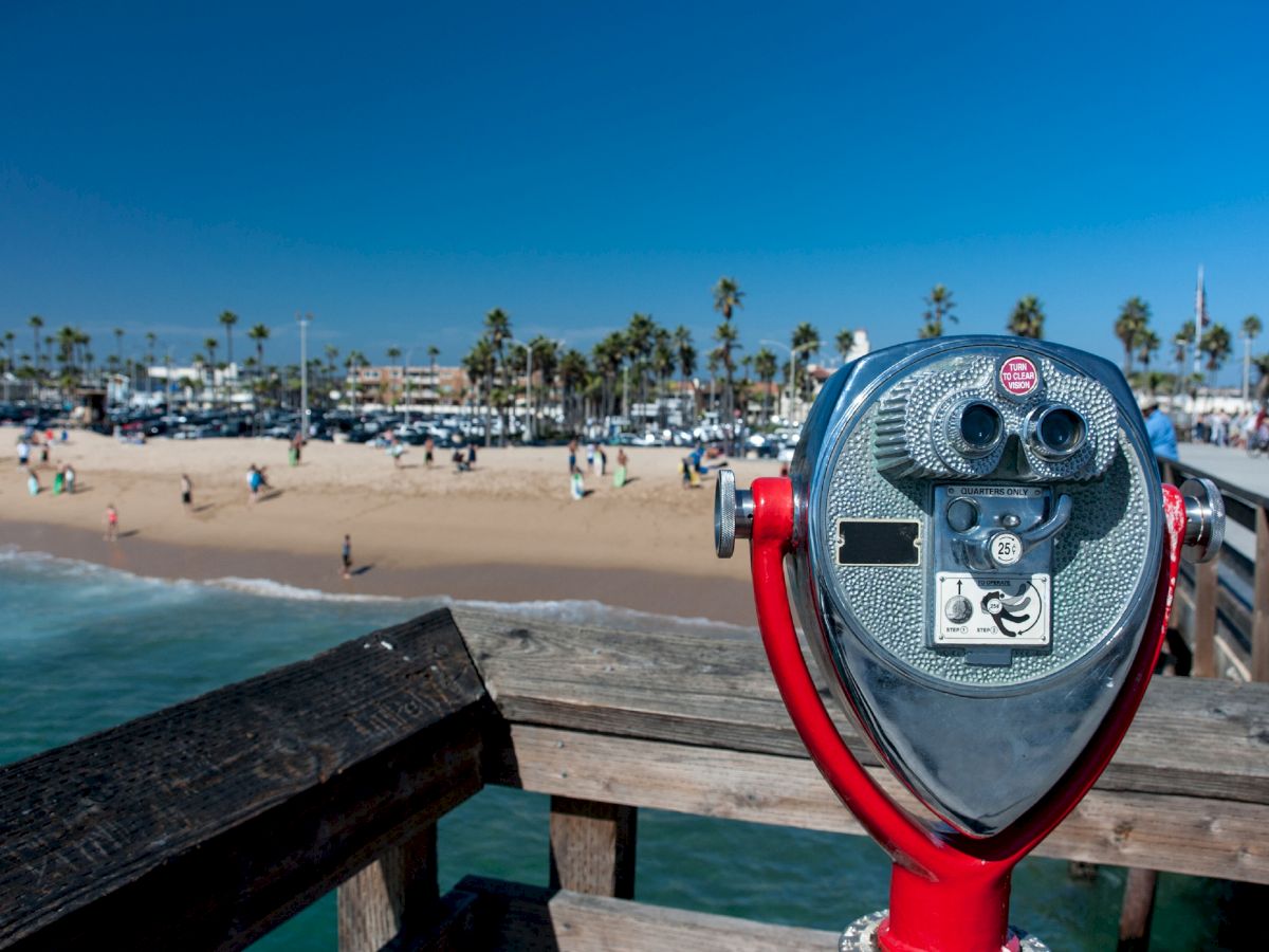 The image shows a viewing binoculars on a pier overlooking a sandy beach with palm trees and people under a clear blue sky, ending the sentence.