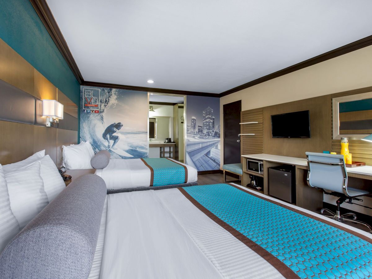 A modern hotel room with two beds, surfer-themed decor, a desk with a chair, a TV, and a mini-fridge, creating a comfortable and functional space.