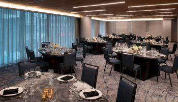 A modern, elegantly set dining room with round tables and chairs, prepared for a formal event or banquet, featuring dim lighting and decorated with flowers.