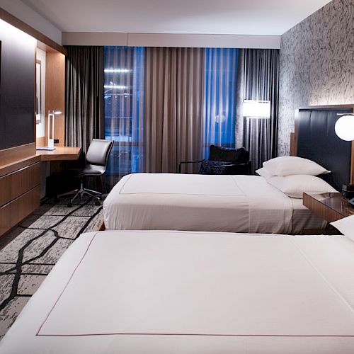 A modern hotel room with two neatly made beds, a large TV on the wall, a desk with a chair, and stylish decor.