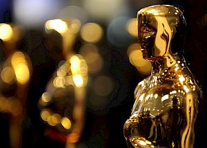 The image shows several golden Oscar statuettes in focus, with a blurred, bokeh background. The iconic trophies symbolize excellence in the film industry.