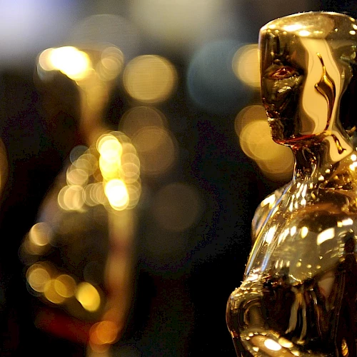 The image shows several golden Oscar statuettes in focus, with a blurred, bokeh background. The iconic trophies symbolize excellence in the film industry.