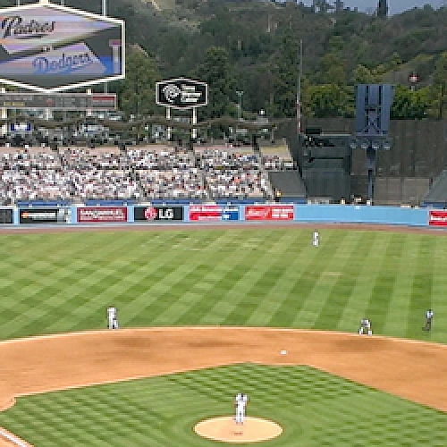 A baseball game is taking place in a stadium with fans in the stands, featuring advertisements and large scoreboards around the field.