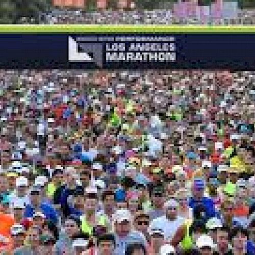 A large crowd of runners is participating in the Los Angeles Marathon, gathered at the starting line under a banner that reads "Los Angeles Marathon.".