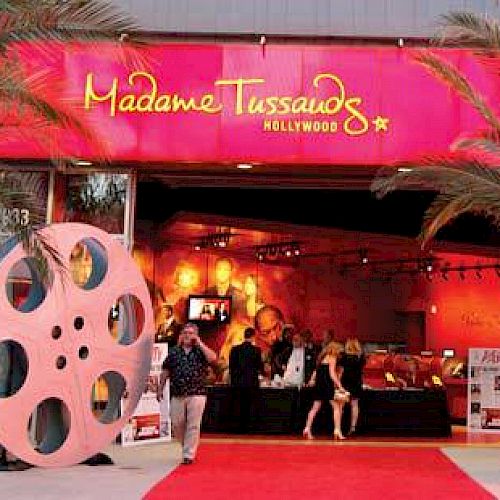 This image shows the entrance to Madame Tussauds Hollywood, with film reel decorations, palm trees, and a red carpet leading to the entrance.
